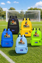 Five backpacks in black, yellow, blue, light blue, and lime green are arranged on a grassy soccer field with a goal in the background. Each backpack features a colorful cartoon graphic and a blue 'Adam' brand patch on the front.